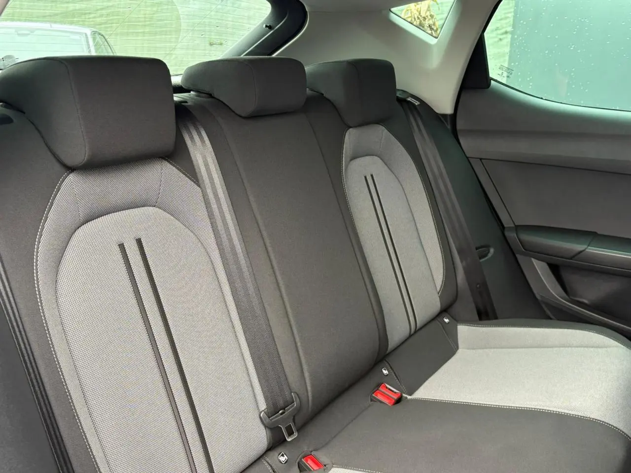 Vue intérieure des sièges arrière en tissu gris et noir du SEAT Leon 2024, avec ceintures de sécurité visibles.