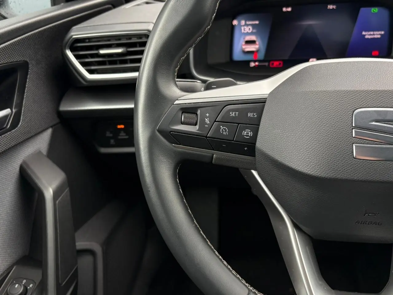 Gros plan sur le volant cuir multifonction et le combiné digital noir du tableau de bord du SEAT Leon 2024.