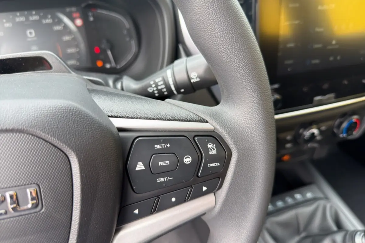 Gros plan sur le volant multifonctions gris d’un Isuzu D-MAX 2026 avec commandes de régulateur et tableau de bord flou.