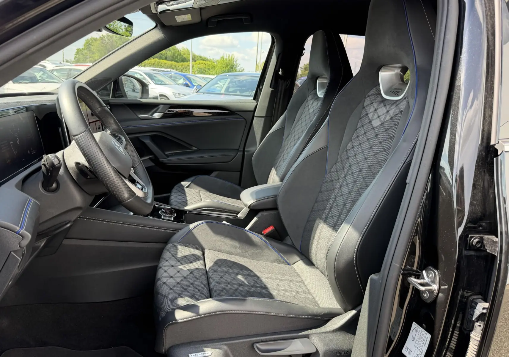 Intérieur avant du Volkswagen Tiguan noir 2025, vue côté conducteur, sièges sport avec surpiqûres bleues et volant cuir multifonction.