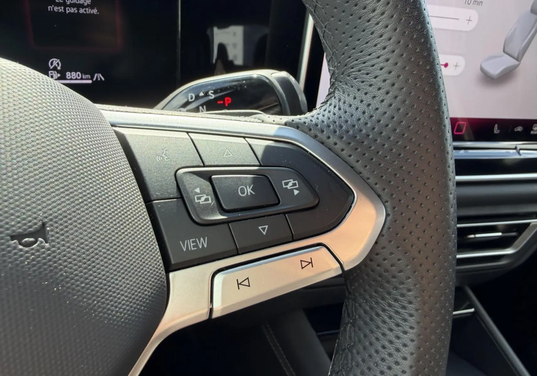 Gros plan sur le côté gauche du volant cuir perforé du Volkswagen Tiguan 2025 avec commandes multifonctions et écran digital en arrière-plan.