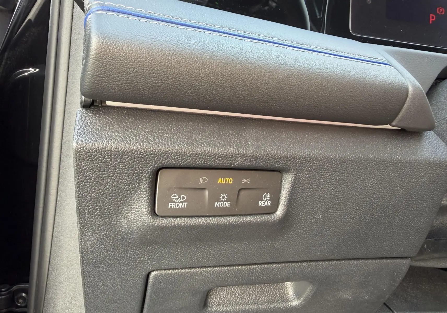 Gros plan sur la commande d’éclairage noire avec mode automatique, sur la partie inférieure gauche du tableau de bord du Volkswagen Tiguan noir.