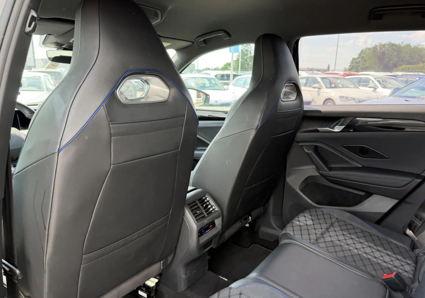 Vue arrière intérieure du Volkswagen Tiguan 2025 noir, sièges avant sport en cuir avec surpiqûres bleues et banquette arrière partiellement visible.