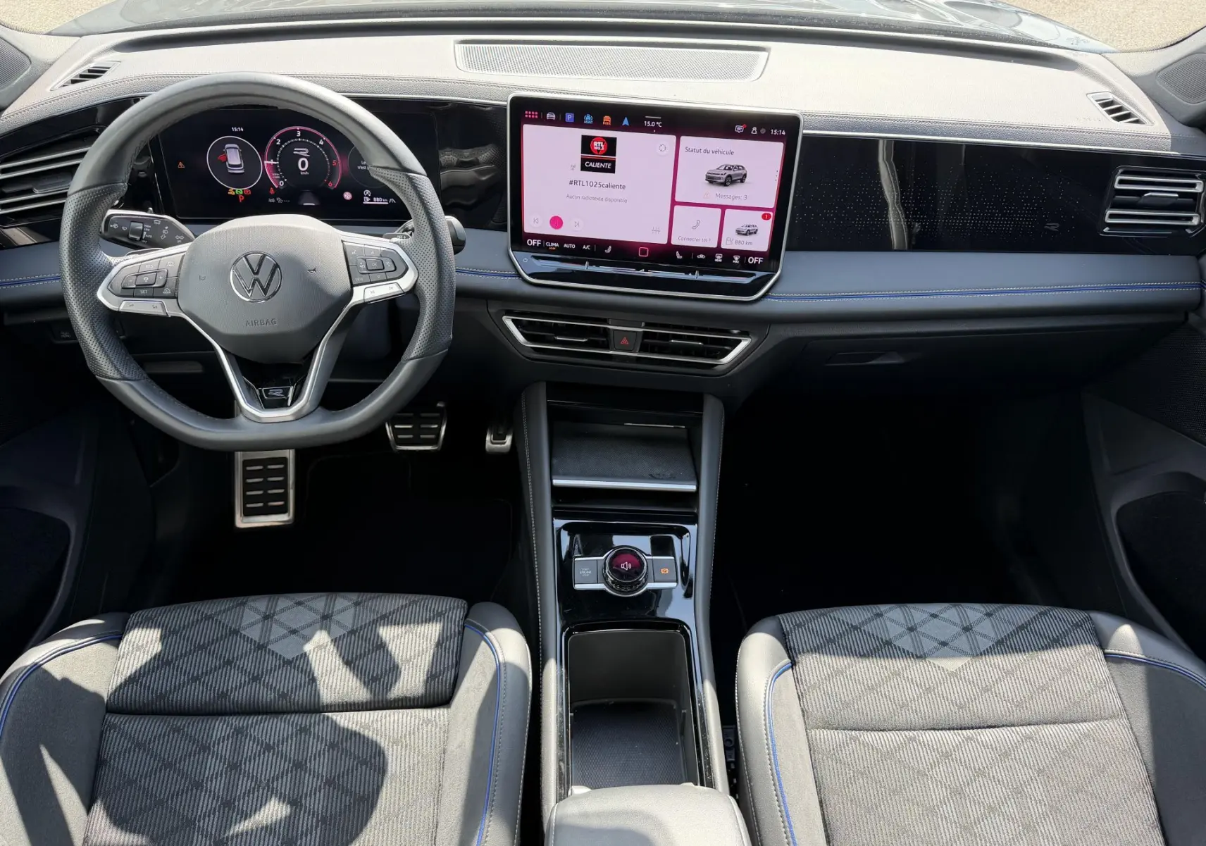 Vue intérieure avant du Volkswagen Tiguan 2025 avec tableau de bord digital, volant sport et sellerie tissu noire à surpiqûres bleues.