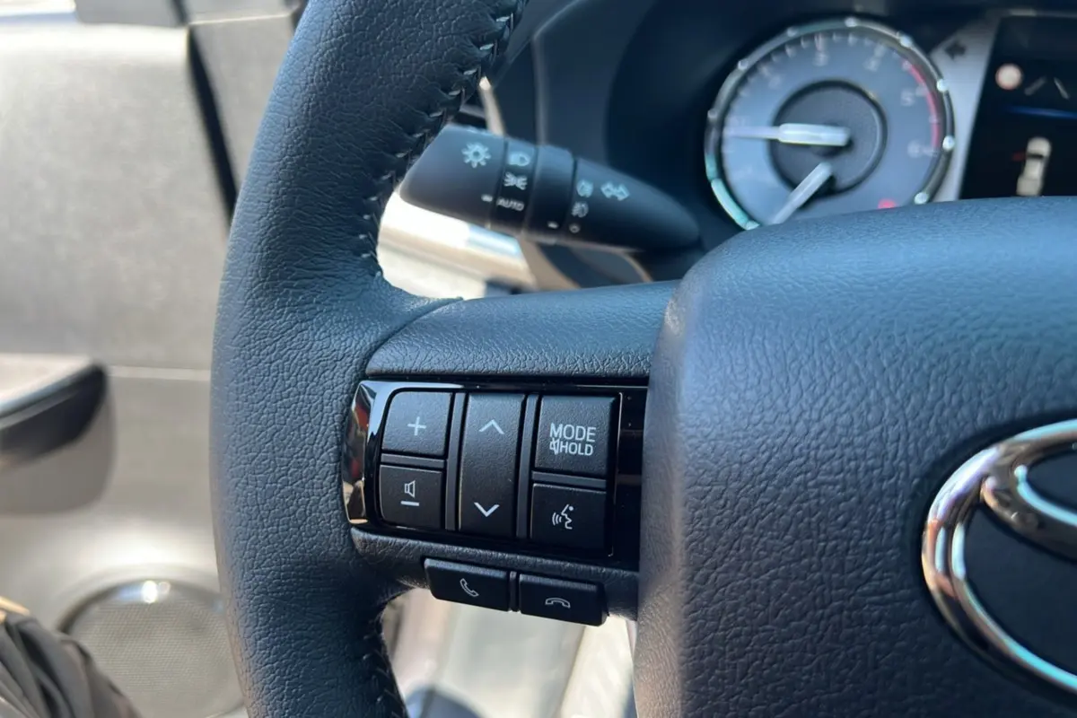 Gros plan sur le volant cuir noir du Toyota Hilux 2026, avec commandes multifonctions visibles côté gauche.