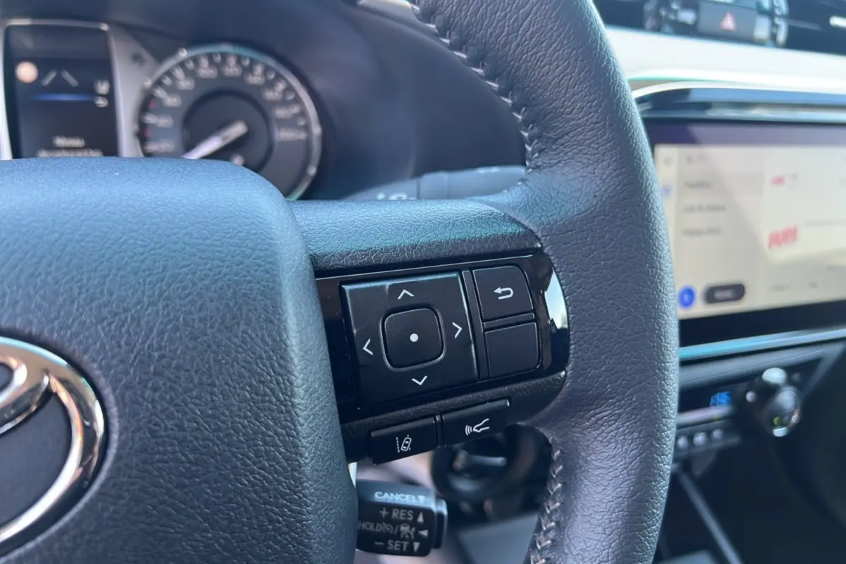 Gros plan sur le volant cuir multifonctions noir du Toyota Hilux 2026 avec tableau de bord et écran tactile visible en arrière-plan.