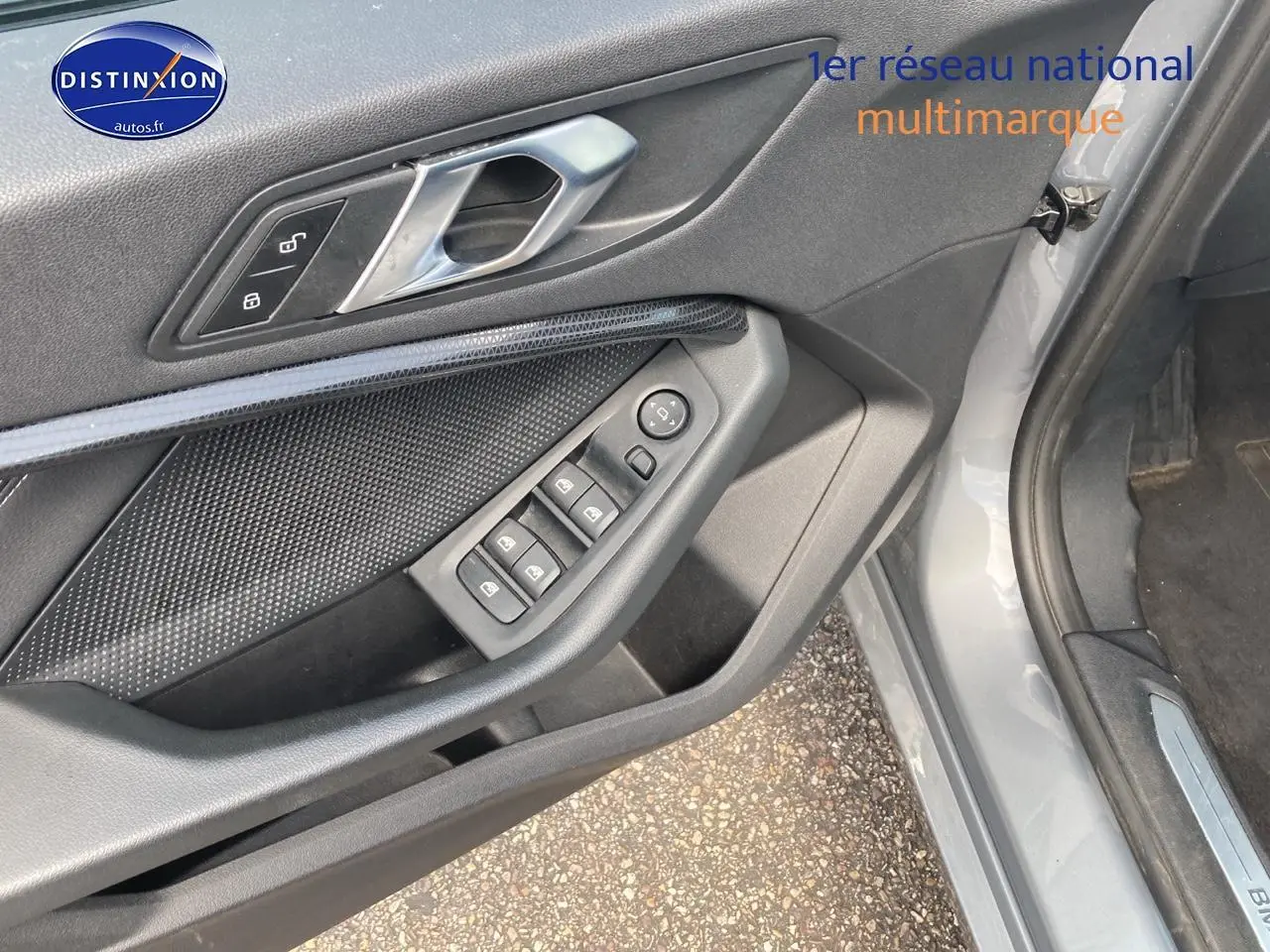 Détail de la porte avant gauche grise d'une BMW Série 1 118i 2023 avec commandes de vitres et verrouillage.