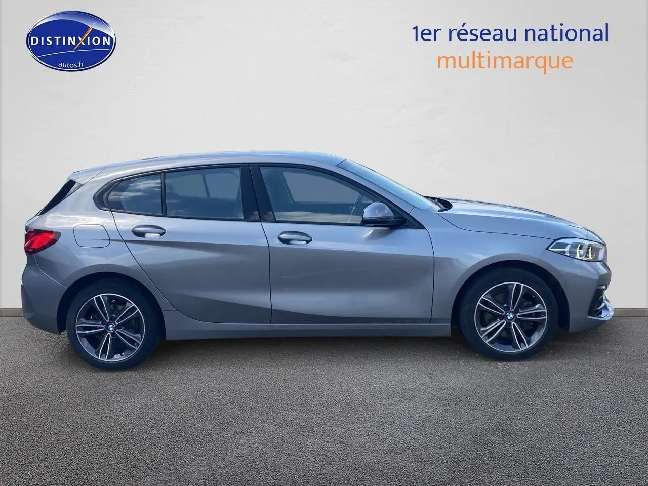 Profil côté gauche d'une BMW Série 1 gris foncé 2023 avec jantes alliage et lignes sportives marquées.