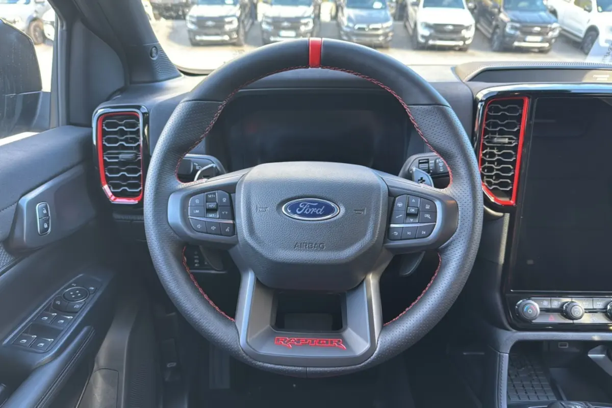 Vue intérieure centrée sur le volant noir du Ford Ranger Raptor 2024 avec surpiqûres rouges et détails rouges autour des aérateurs.