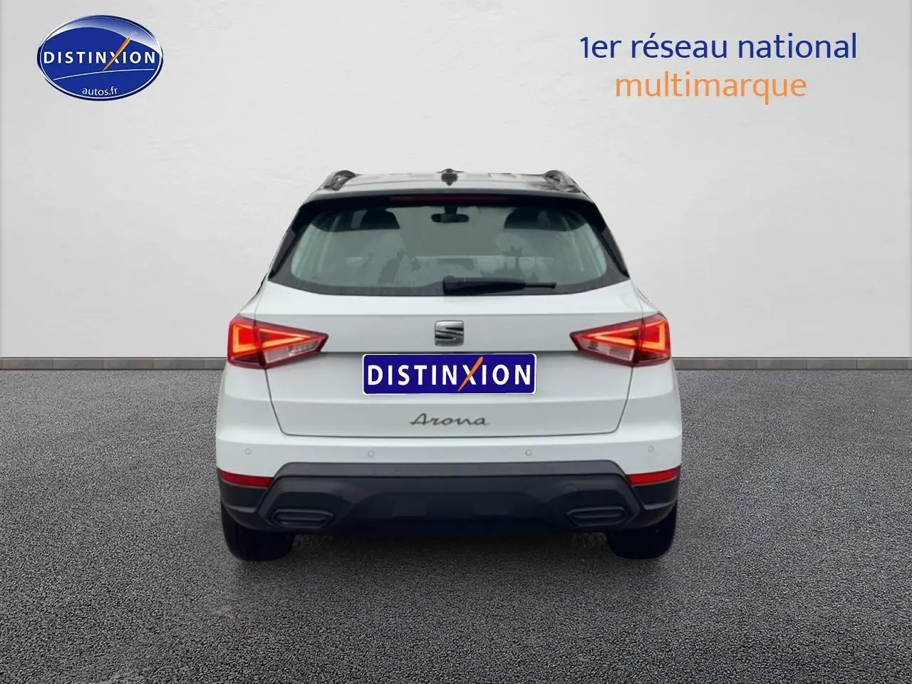 Vue arrière d'un SEAT Arona blanc Nevada avec feux allumés et logos distinctifs sur un sol gris.