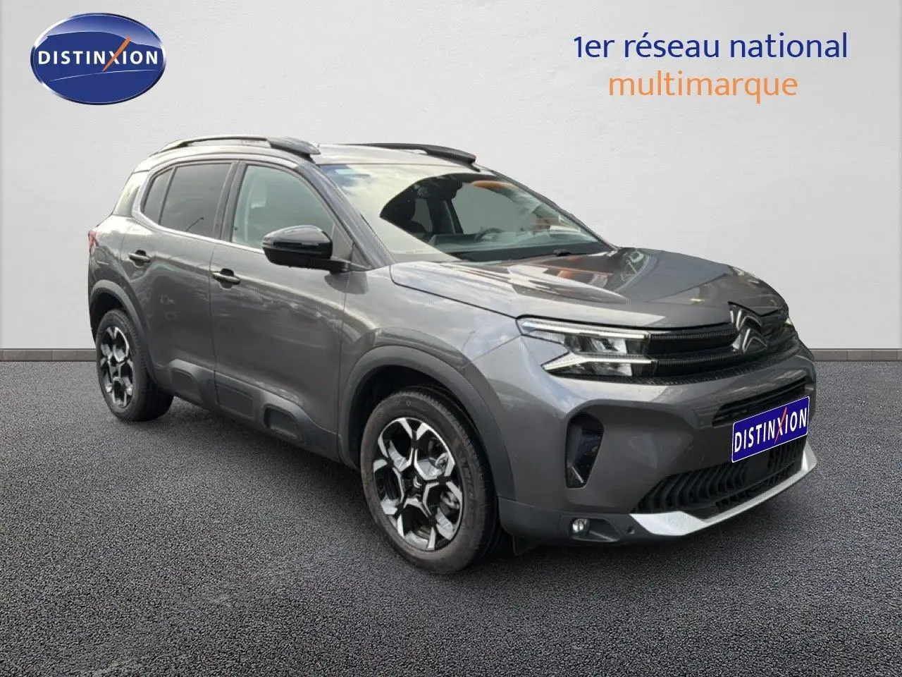 Vue 3/4 avant droite d'un Citroën C5 Aircross gris platinium métallisé avec jantes bi-ton et barres de toit.