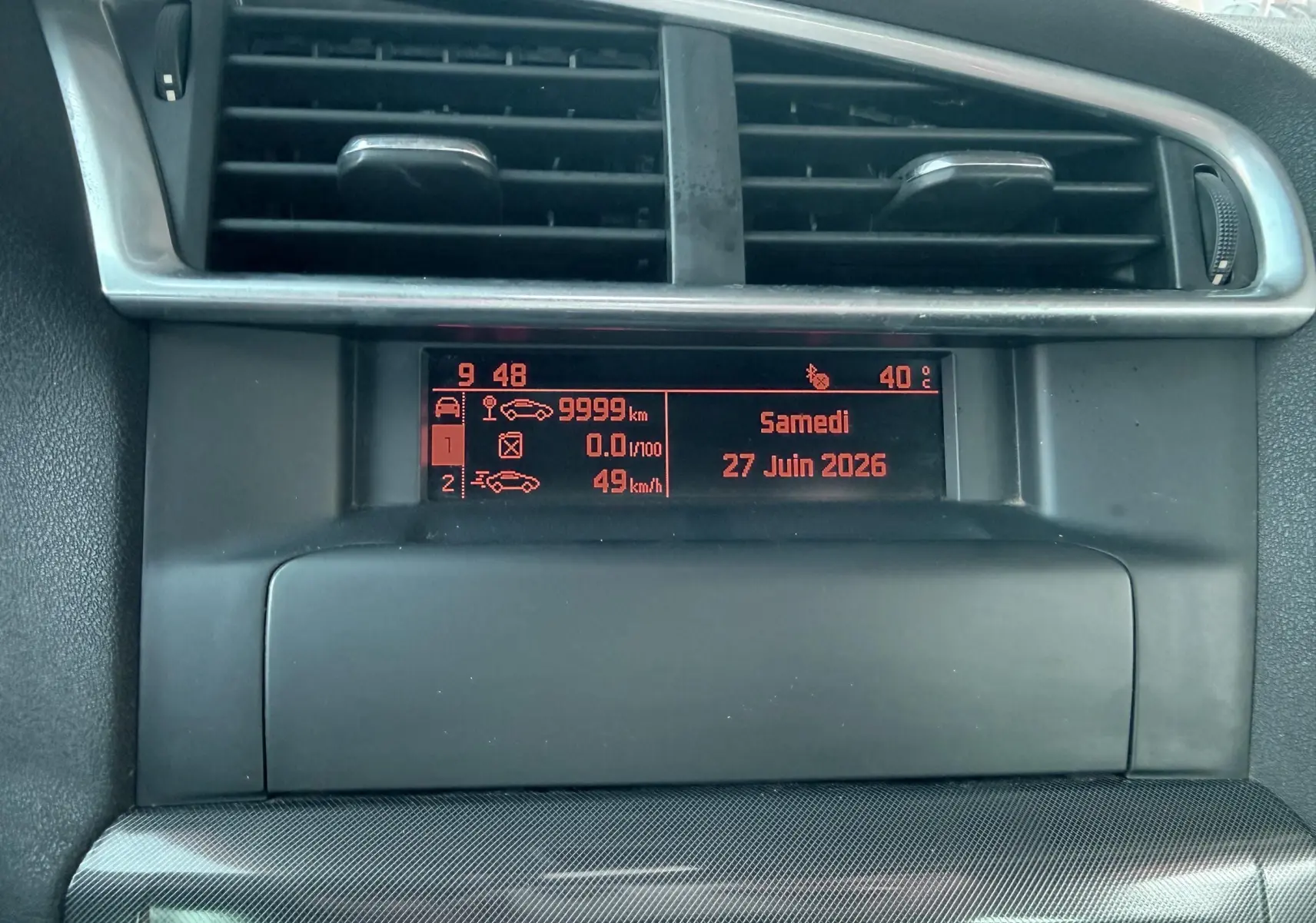 Affichage central du tableau de bord de la Citroën C4 gris, montrant l'horloge, la date et les informations de conduite.