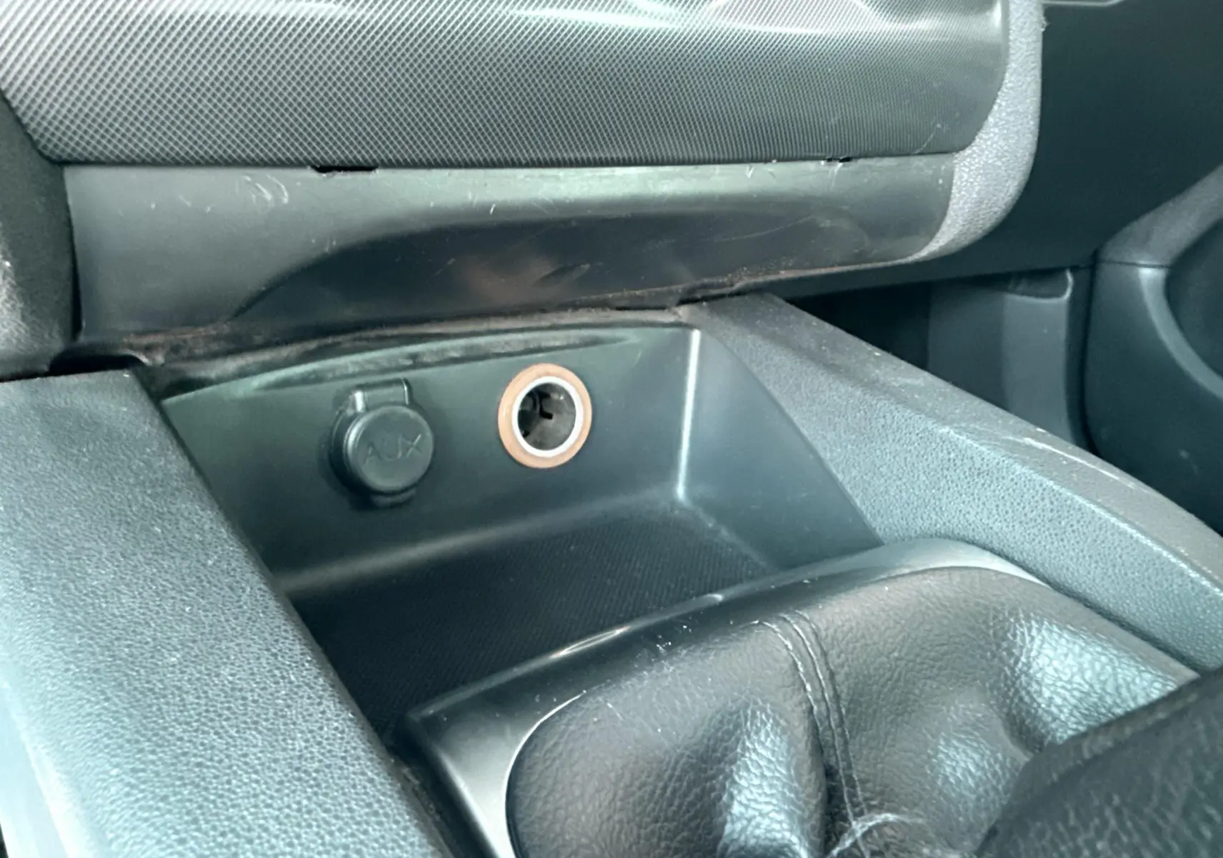 Gros plan sur la console centrale noire de la Citroën C4 2011, montrant la prise AUX et l’allume-cigare.