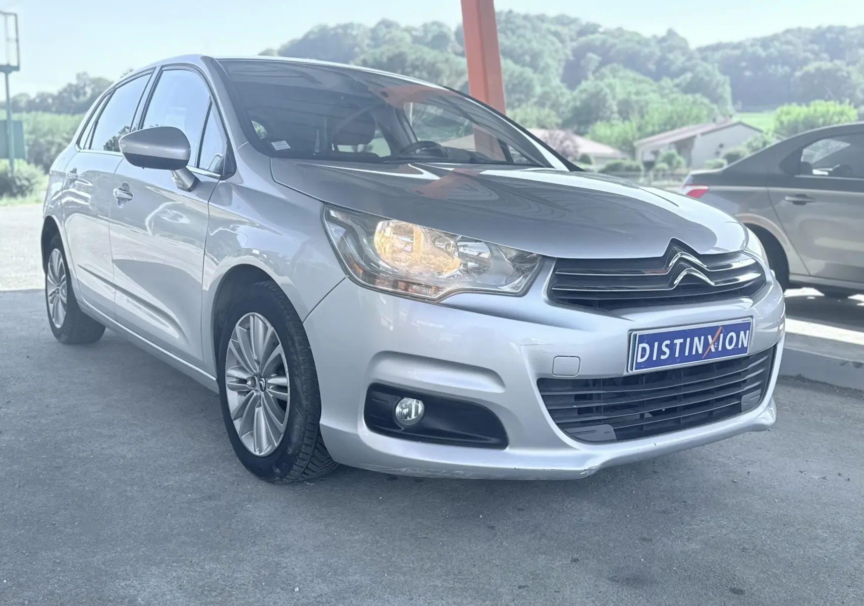 Citroën C4 gris vue 3/4 avant droit avec phare allumé, calandre noire et jantes alliage 16 pouces.
