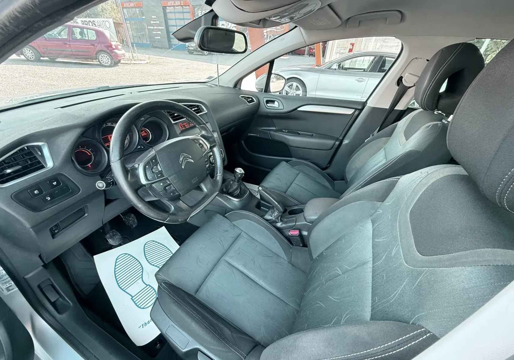 Vue intérieure côté conducteur de la Citroën C4 gris, montrant le volant, la boîte manuelle et les sièges tissu noirs.