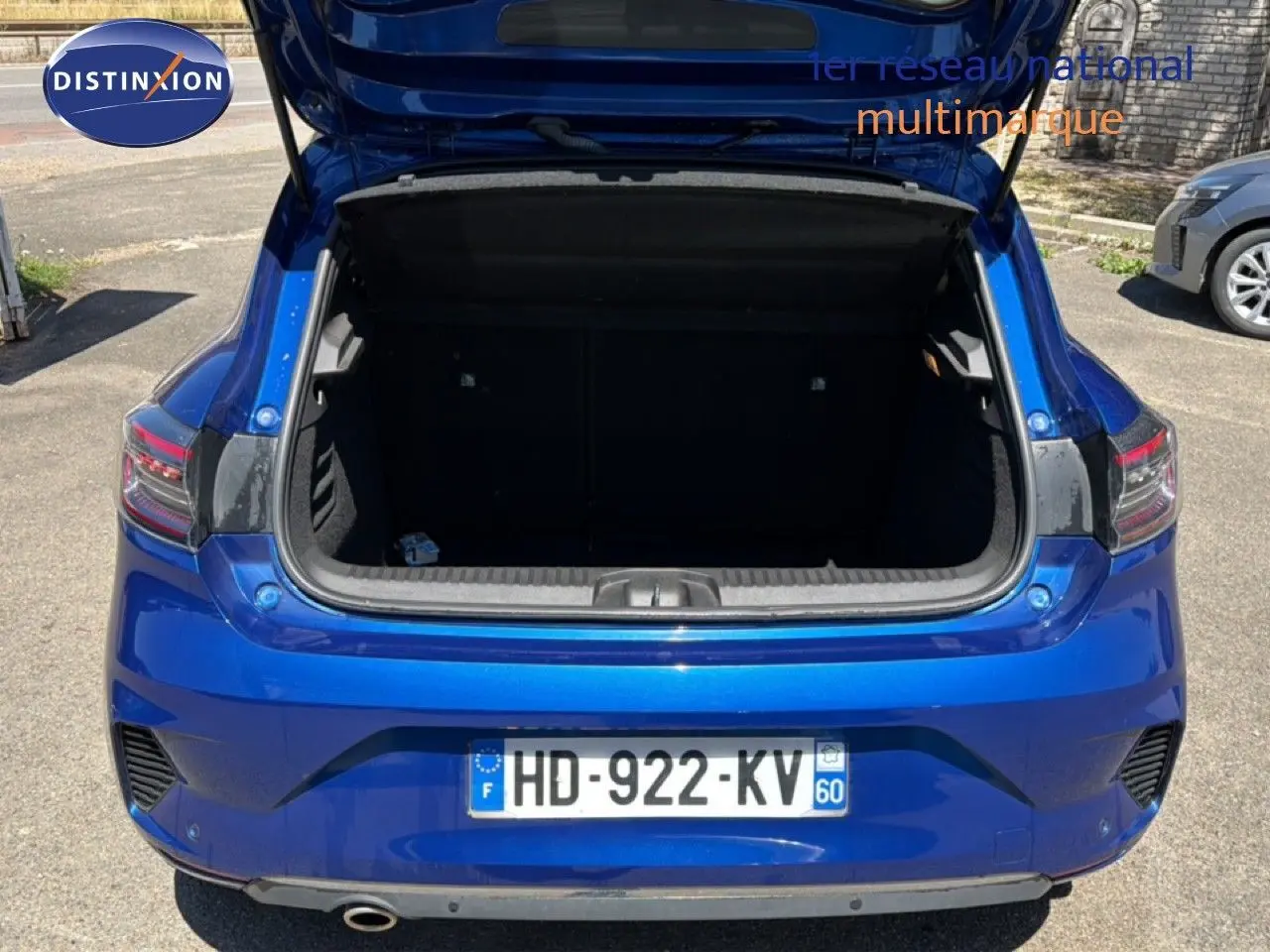 Vue arrière d'une Renault Clio 2025 bleu iron metal avec coffre ouvert, montrant les feux arrière et la plaque d'immatriculation.