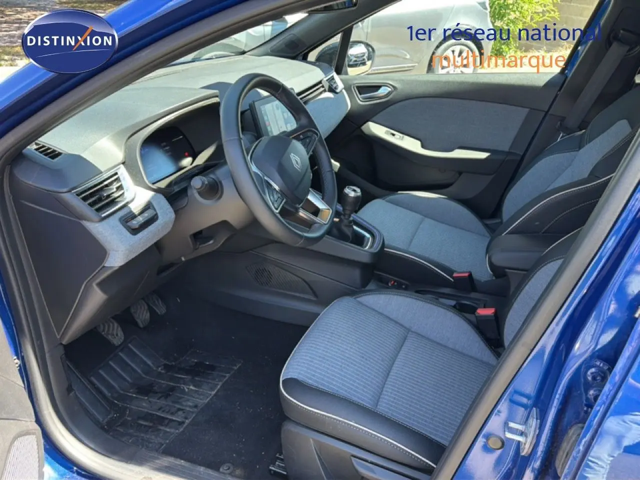 Vue intérieure côté conducteur d'une Renault Clio 2025 bleu Iron Metal, sièges tissu gris et volant cuir multifonction.