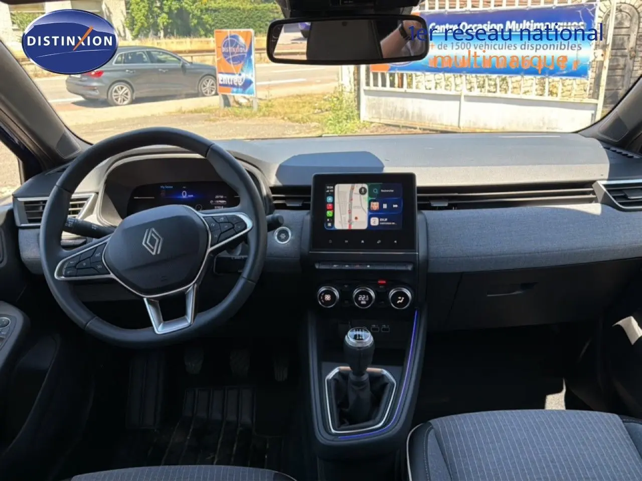 Vue intérieure avant de la Renault Clio 2025 avec tableau de bord moderne, écran tactile et volant multifonction.