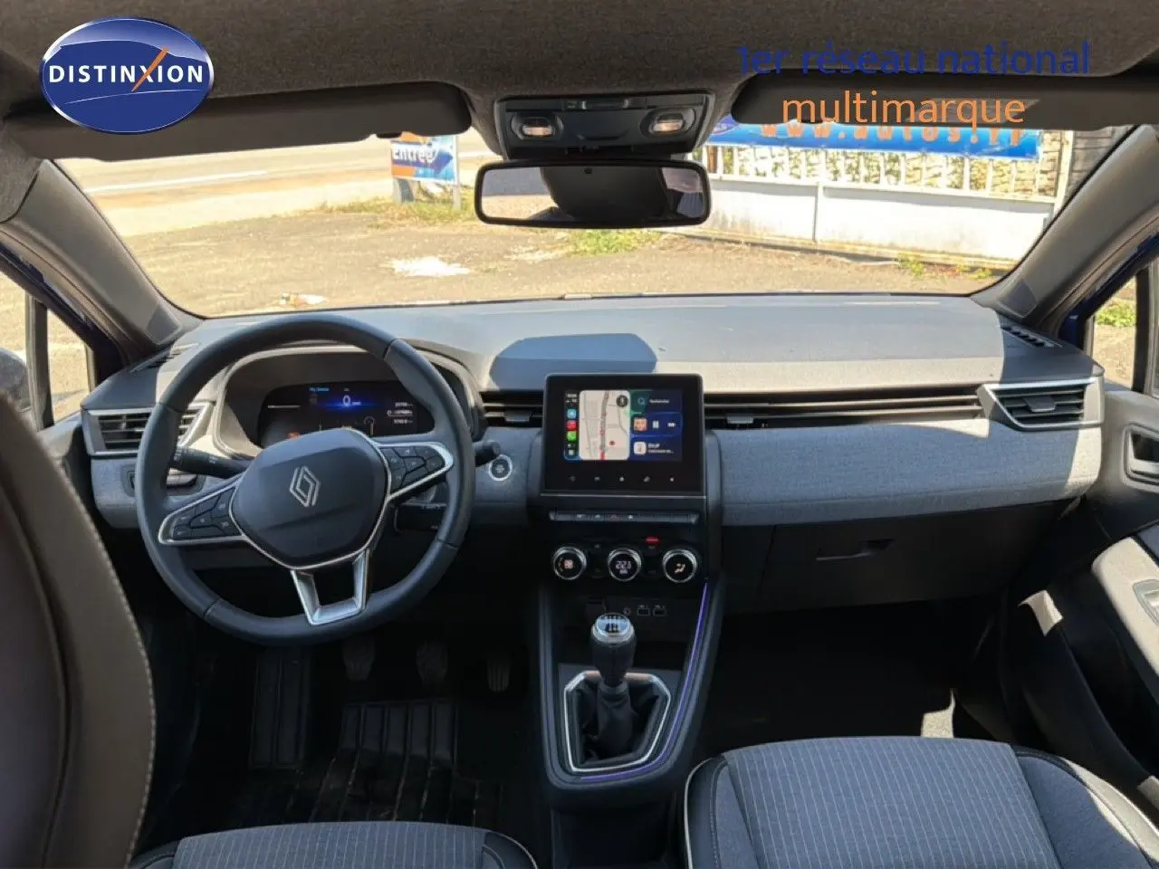 Vue intérieure avant de la Renault Clio 2025 bleu iron metal, tableau de bord moderne avec écran tactile et volant multifonction.
