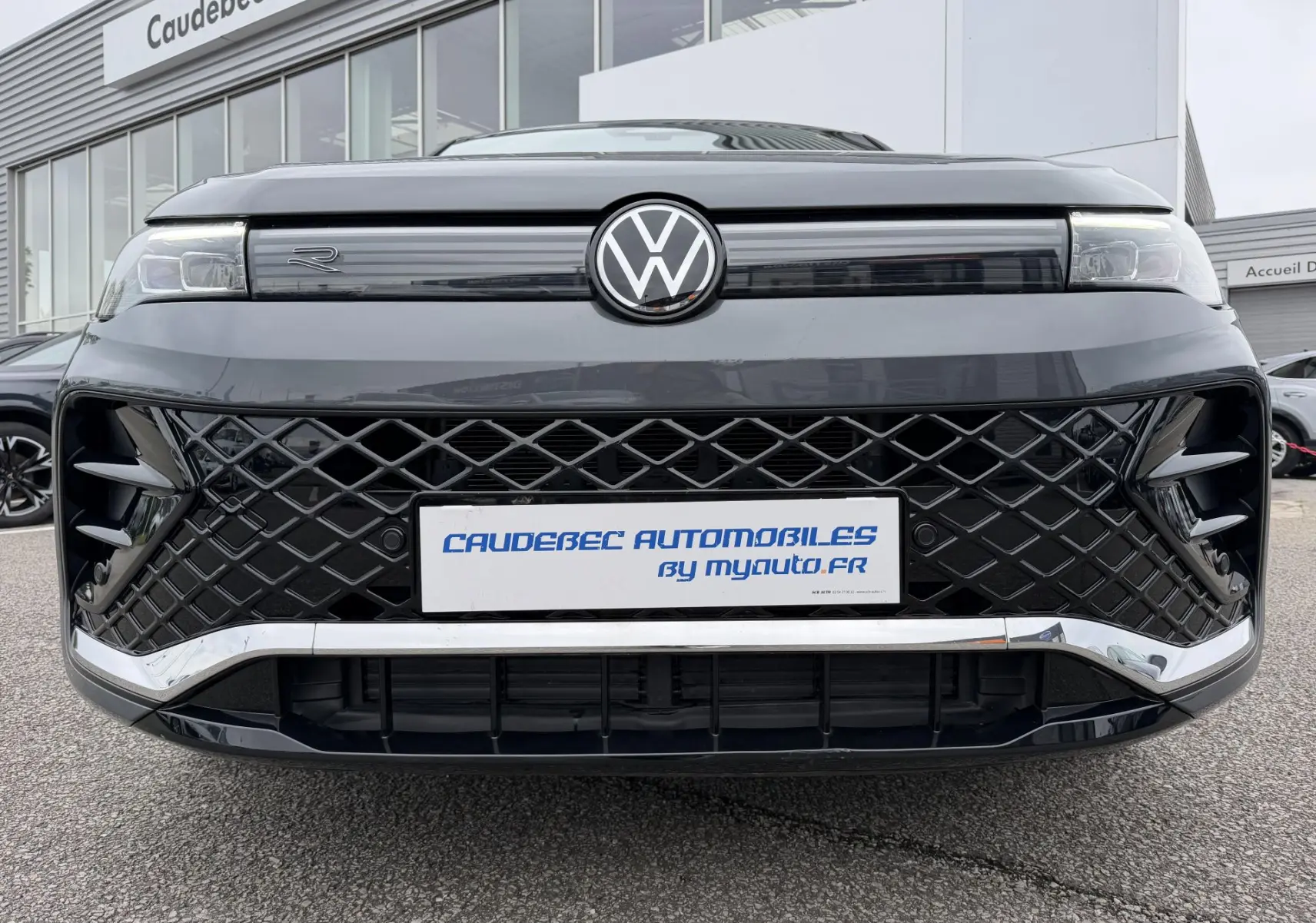 Vue frontale rapprochée du Volkswagen Tiguan gris 2025 avec calandre noire à motif losange et logo VW central lumineux.