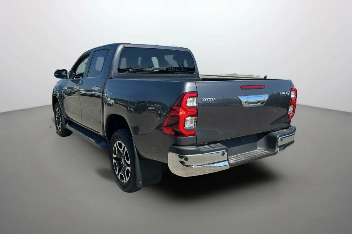 Toyota Hilux 4x4 gris atlas vu en 3/4 arrière droit, avec jantes alu 18 pouces et marchepieds visibles.