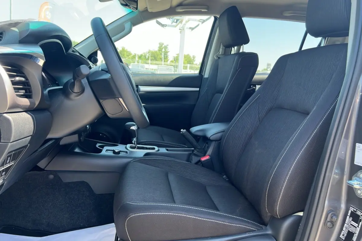 Vue intérieure côté gauche du Toyota Hilux 2026 gris atlas, montrant les sièges avant en tissu et la console centrale.