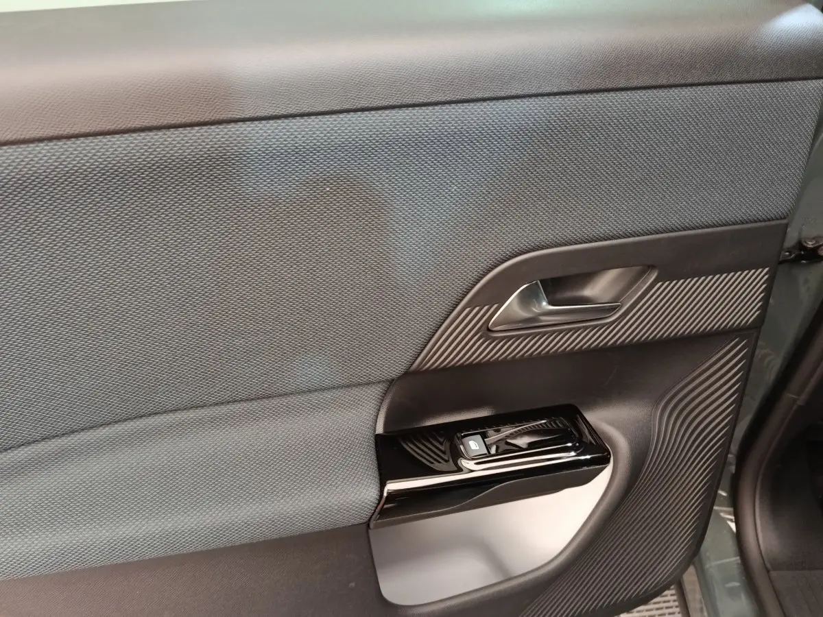 Vue intérieure côté gauche de la porte avant d’une Citroën C5 hybride 2026 avec tissu gris et insert plastique noir texturé.
