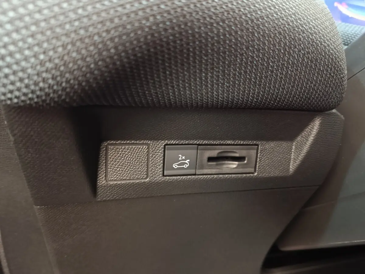 Gros plan sur le bouton d'ouverture du coffre noir situé sous le siège d'une Citroën C5 hybride verte.
