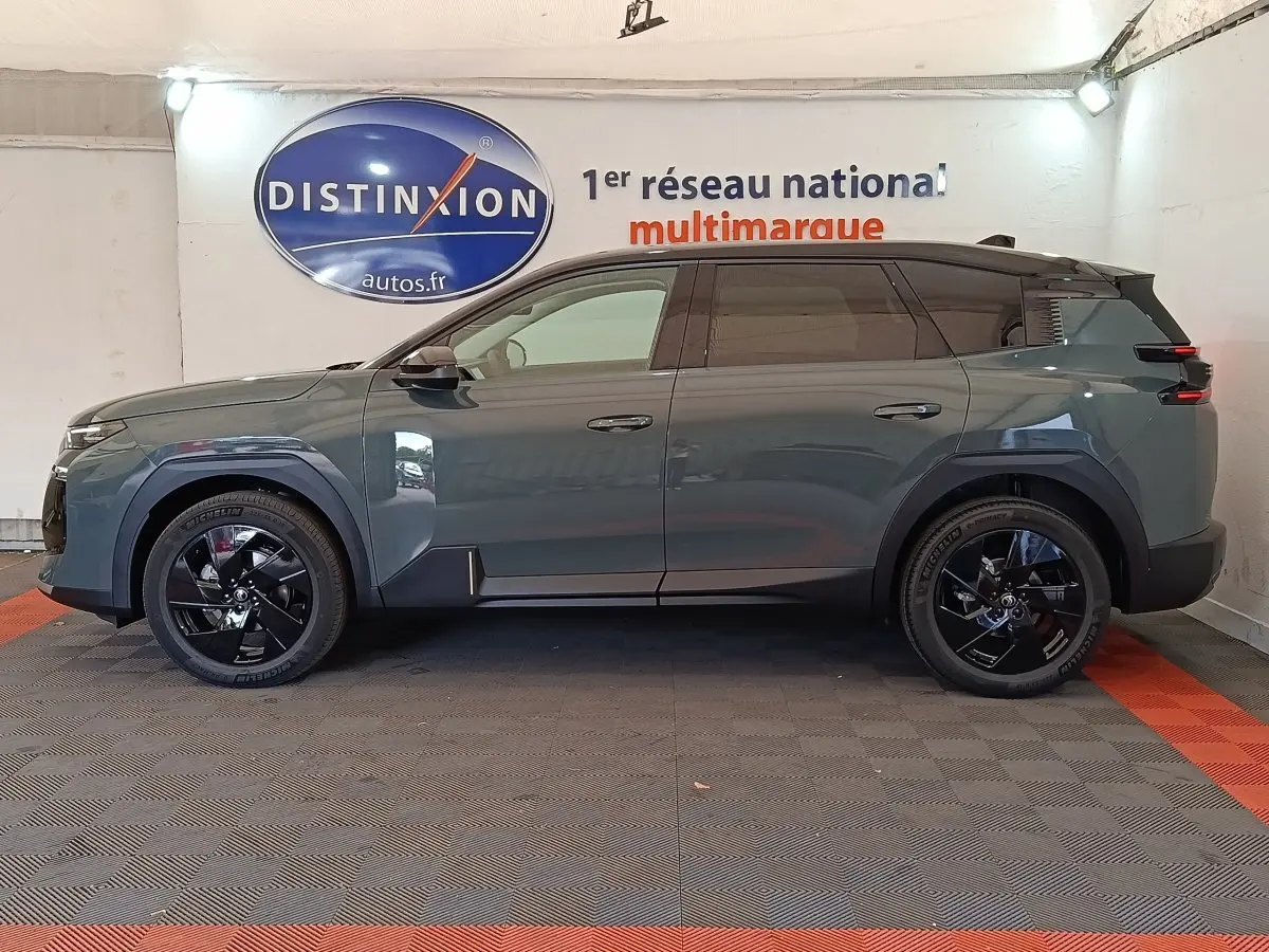 Vue de profil côté gauche d'un Citroën C5 hybride vert avec jantes noires et toit noir en intérieur showroom.