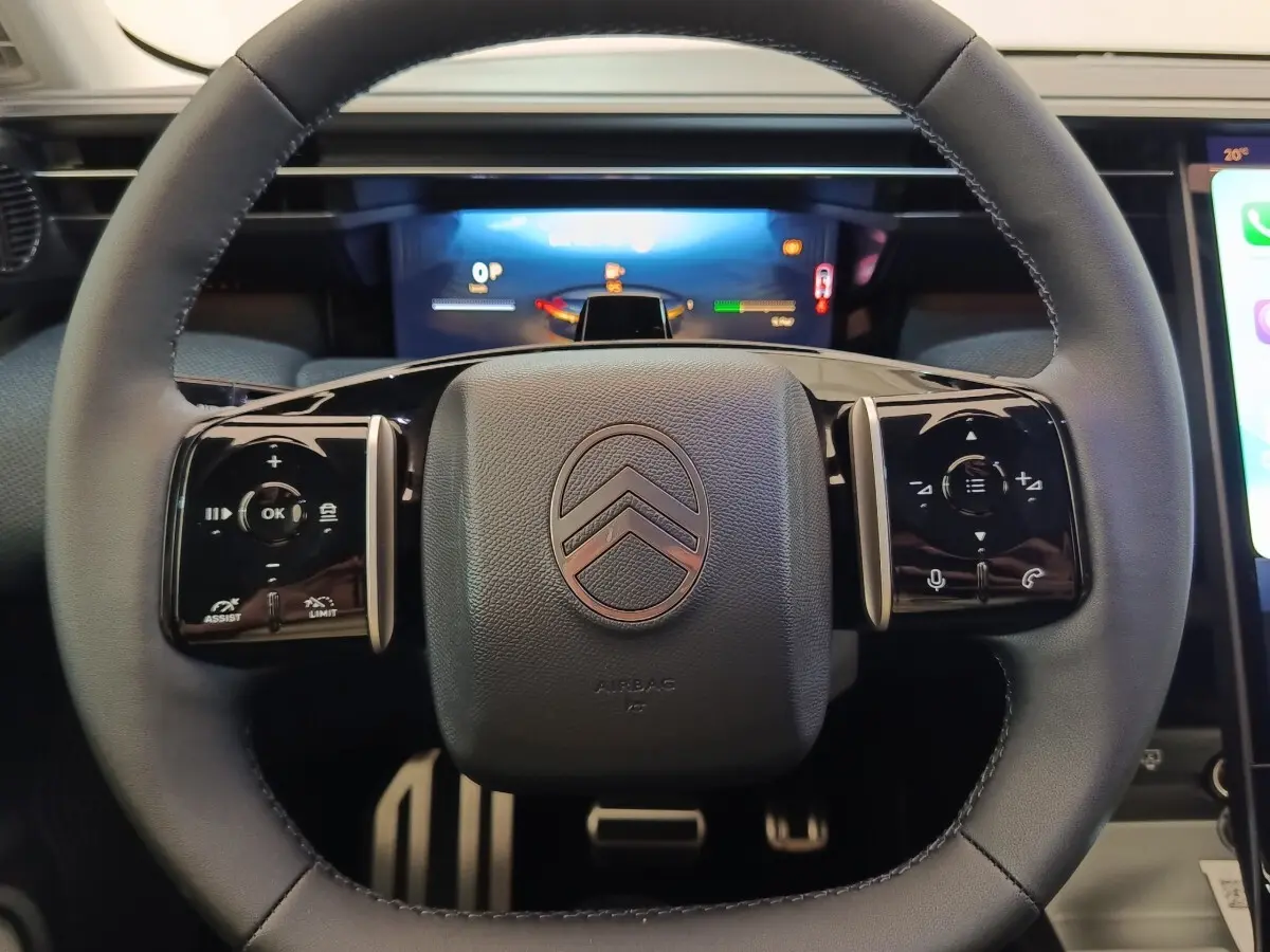 Vue rapprochée du volant noir de la Citroën C5 hybride 2026 avec commandes multifonctions et logo central.