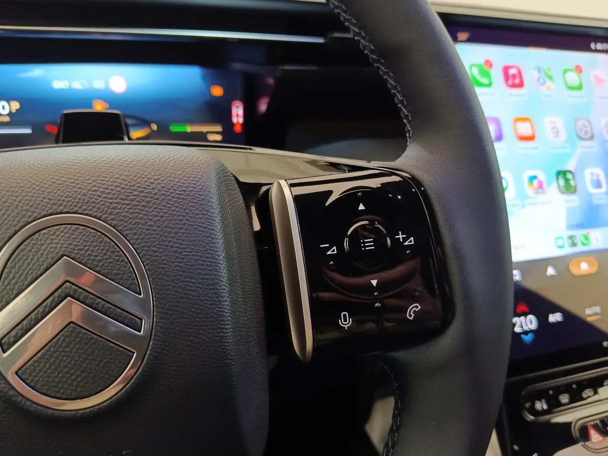 Gros plan sur le volant cuir noir de la Citroën C5 Hybride 2026 avec commandes multifonctions et écran tactile en arrière-plan.