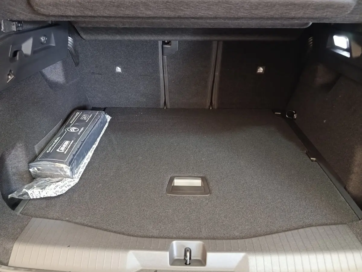 Coffre spacieux de Citroën C5 Hybride 2026 vu de face, revêtement noir avec kit de sécurité sur le côté gauche.