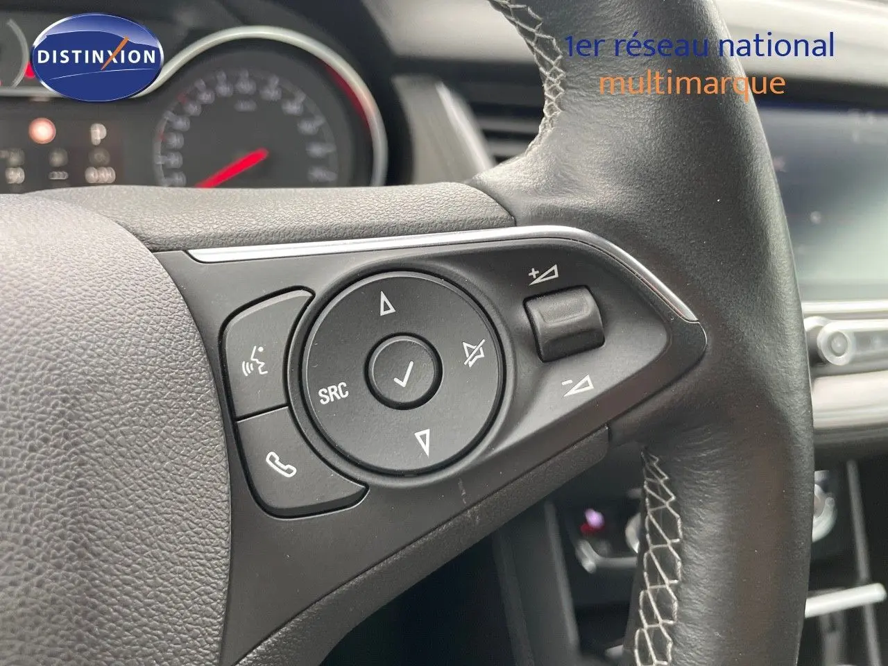 Gros plan sur les commandes au volant en cuir noir de l'Opel Grandland X Golden Sunstone, tableau de bord flou en arrière-plan.