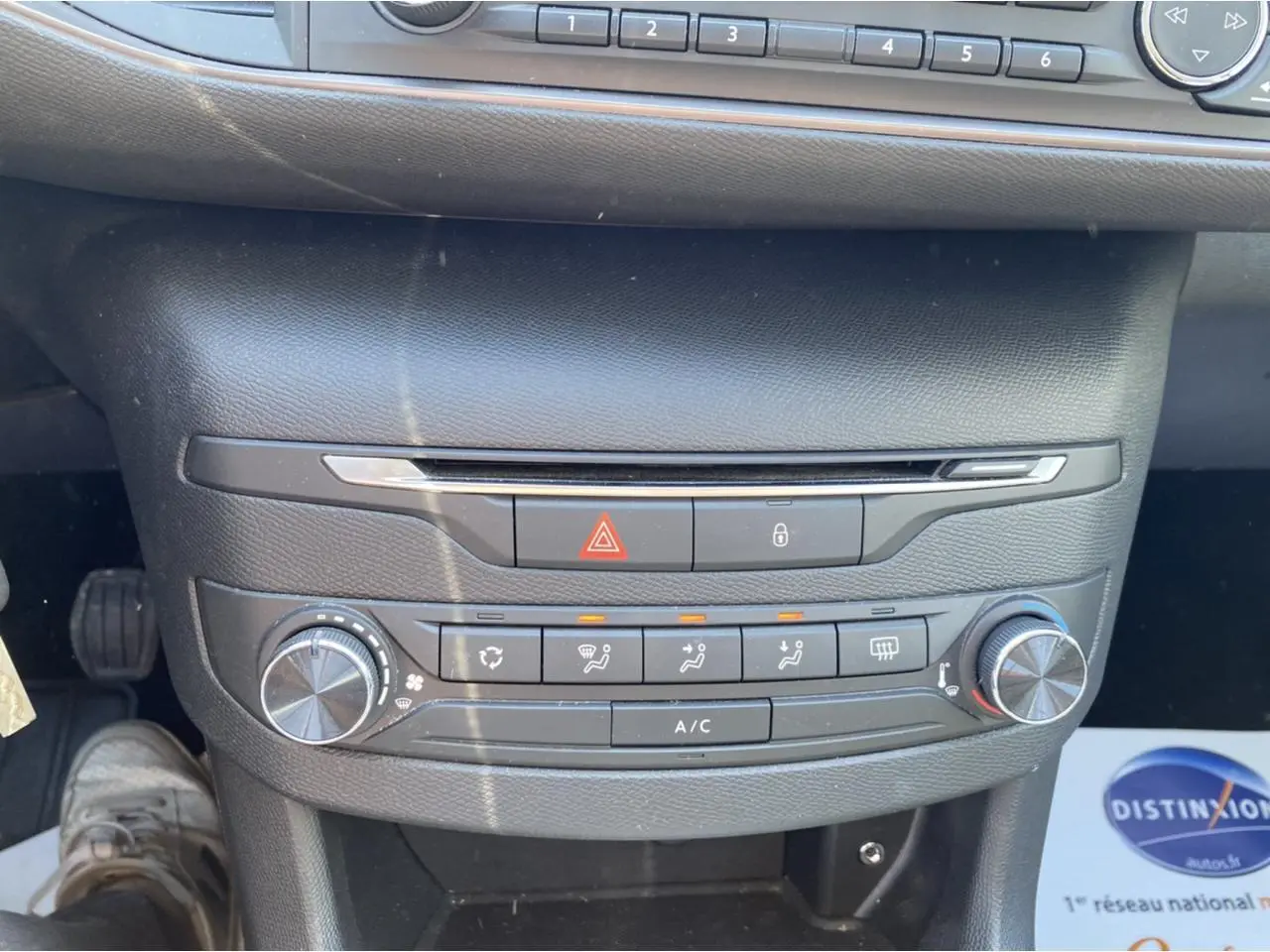 Tableau de bord central de Peugeot 308 SW gris clair, avec commandes de climatisation manuelle et boutons d'alerte visibles.