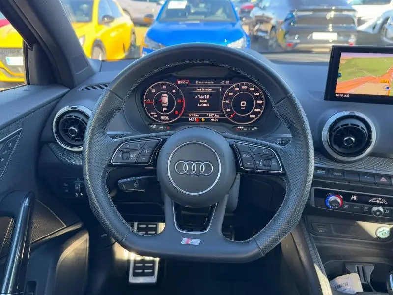 Vue intérieure centrée sur le volant sport en cuir de l'Audi Q2 noir Mythic, avec tableau de bord numérique et écran GPS visible.
