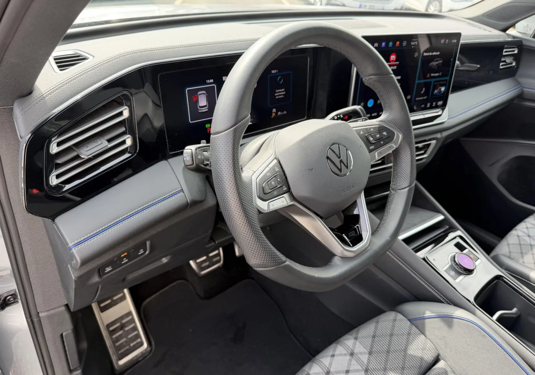 Vue intérieure côté conducteur du Volkswagen Tiguan 2025, volant cuir noir, tableau de bord digital et sièges gris à surpiqûres bleues.