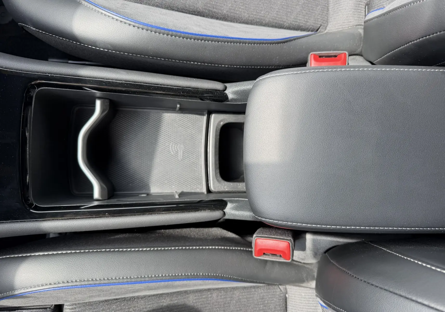Vue plongeante sur la console centrale du Volkswagen Tiguan gris, avec accoudoir cuir noir et surpiqûres blanches.
