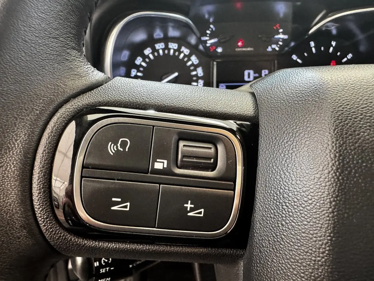 Gros plan sur le volant cuir multifonctions côté gauche de la Citroën C3 gris foncé avec commandes vocales et volume.