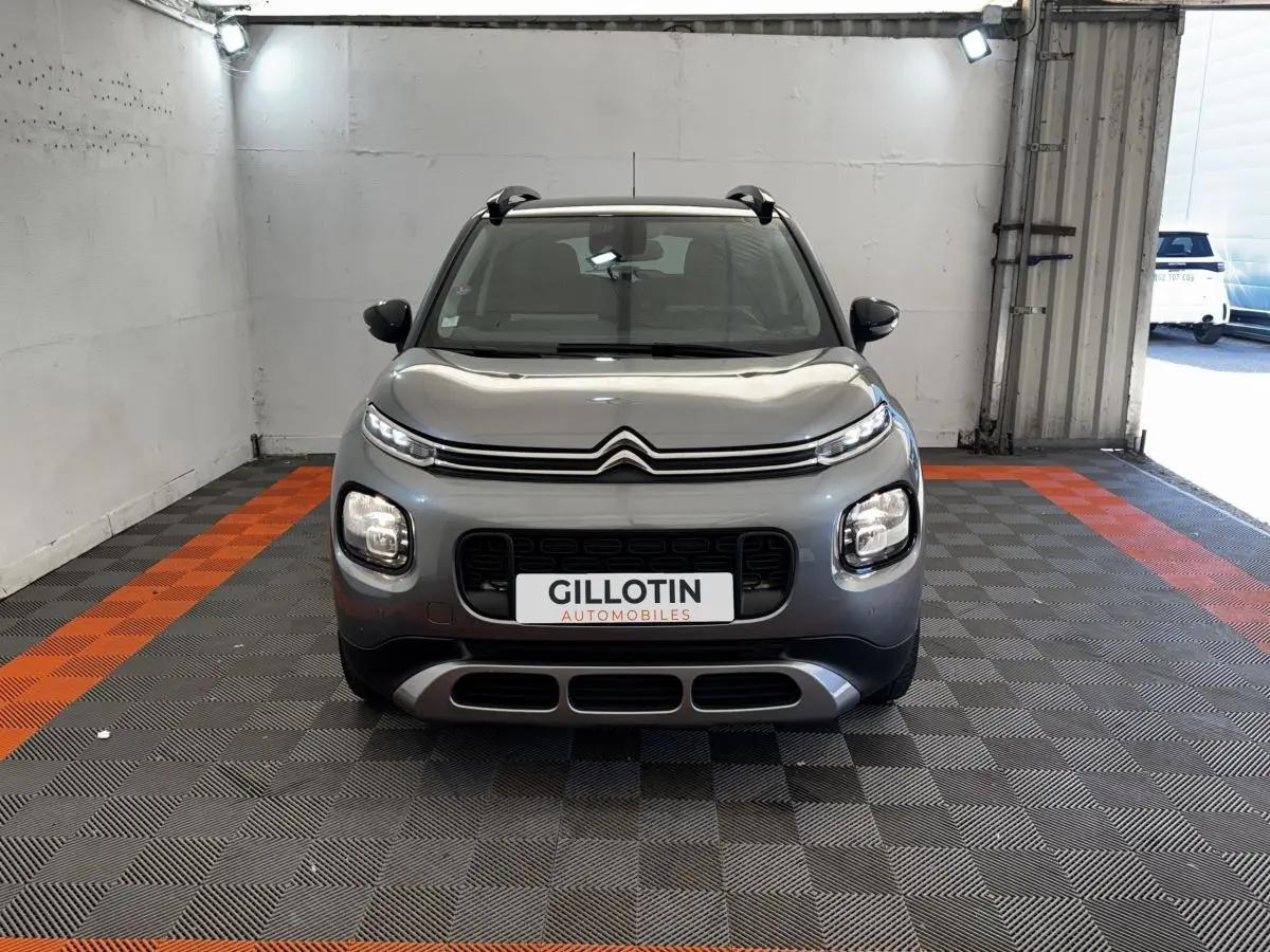 Vue frontale d'une Citroën C3 gris foncé avec calandre noire et feux LED, dans un garage éclairé.