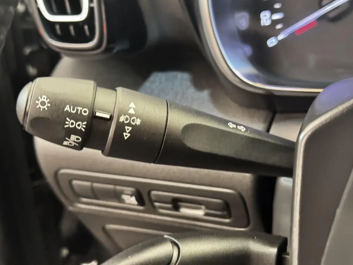 Gros plan sur la commande des phares et clignotants à gauche du volant dans une Citroën C3 gris foncé de 2019.