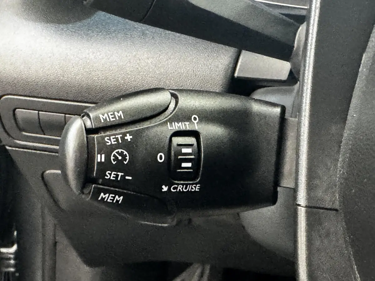 Gros plan sur la commande de régulateur de vitesse noire à gauche du volant dans une Citroën C3 gris foncé 2019.