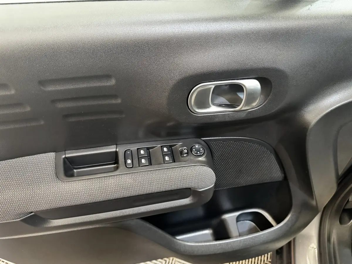 Gros plan sur la porte intérieure côté conducteur de la Citroën C3 gris foncé, avec commandes des vitres et poignée métallique.