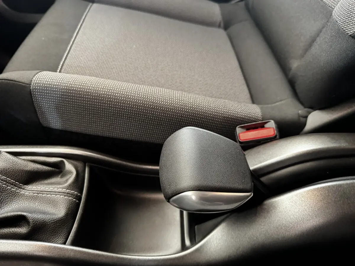 Gros plan sur le levier de frein à main noir et la console centrale, avec siège tissu gris foncé à côté dans une Citroën C3.