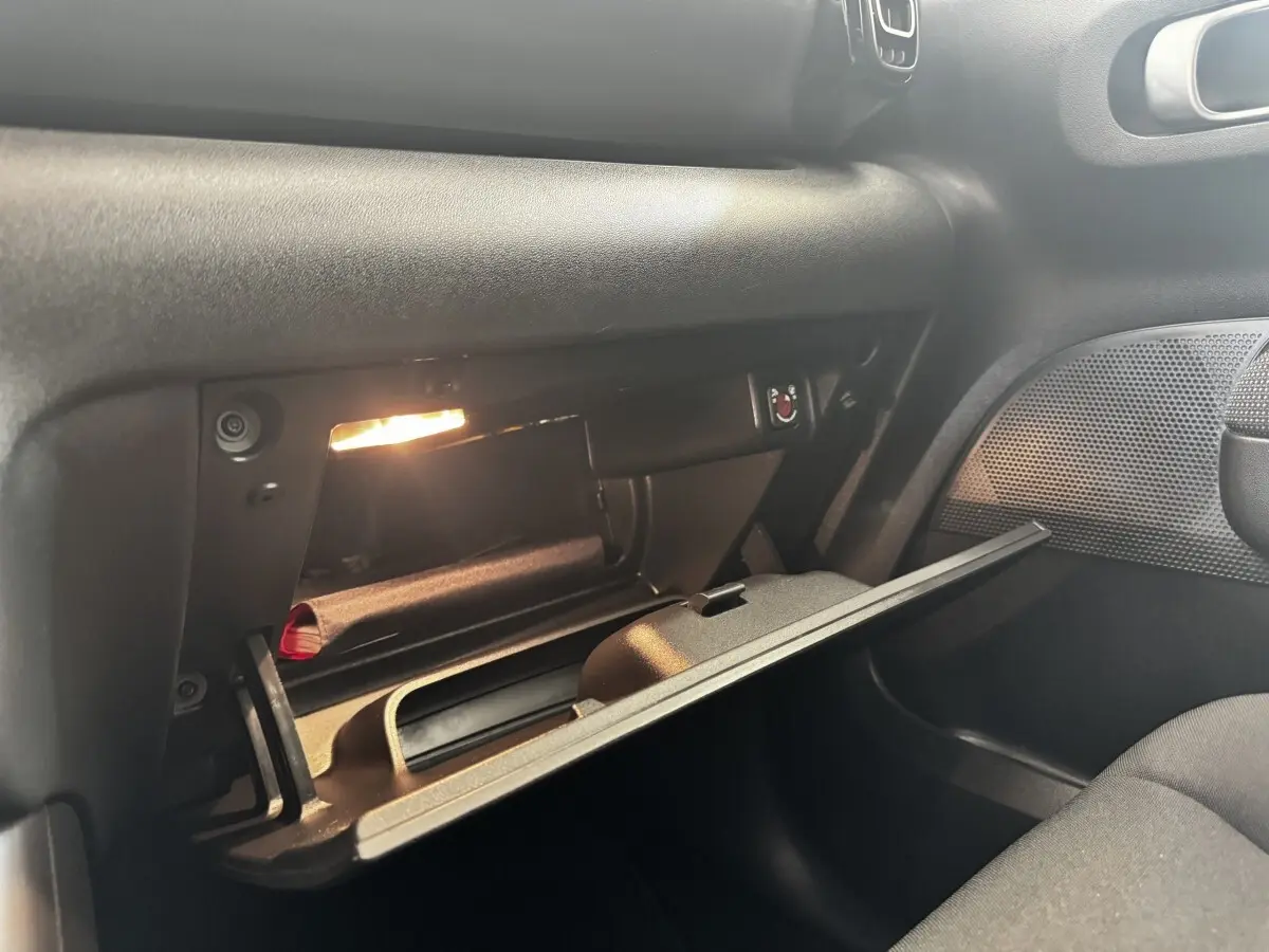 Boîte à gants ouverte côté passager de la Citroën C3 gris foncé, éclairée et montrant un rangement intérieur.
