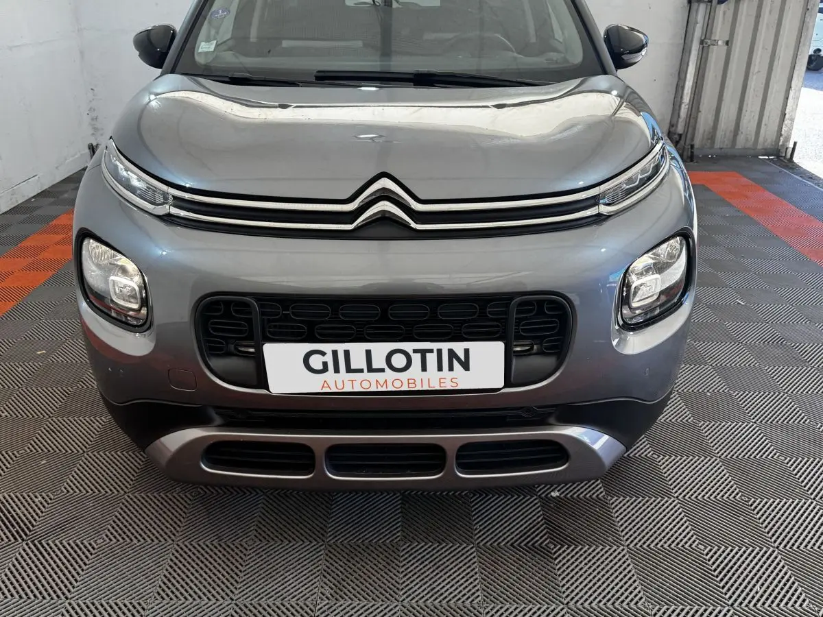 Vue avant d'une Citroën C3 gris foncé avec calandre noire et phares LED distinctifs, en intérieur showroom.
