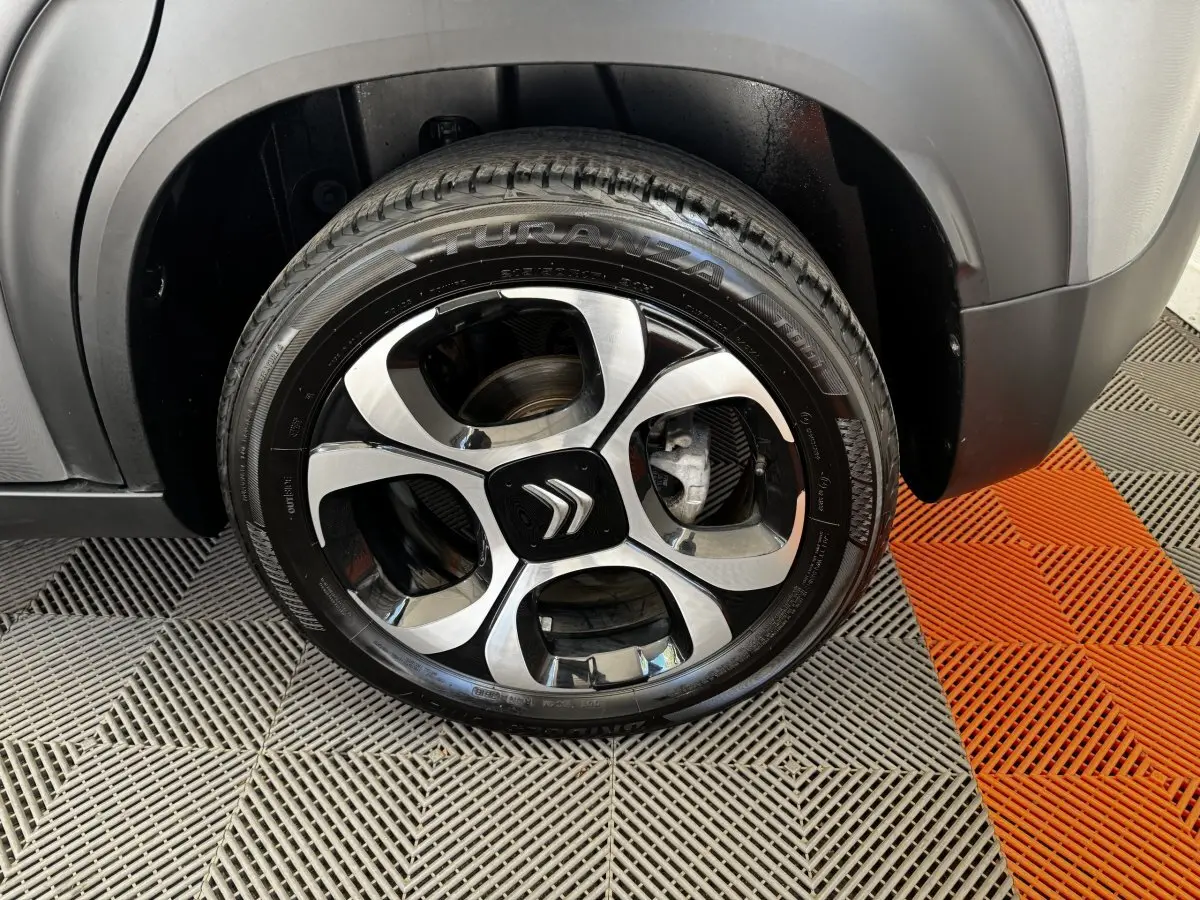 Gros plan sur la roue avant droite d'une Citroën C3 gris foncé avec jante alliage noire et argentée au design distinctif.