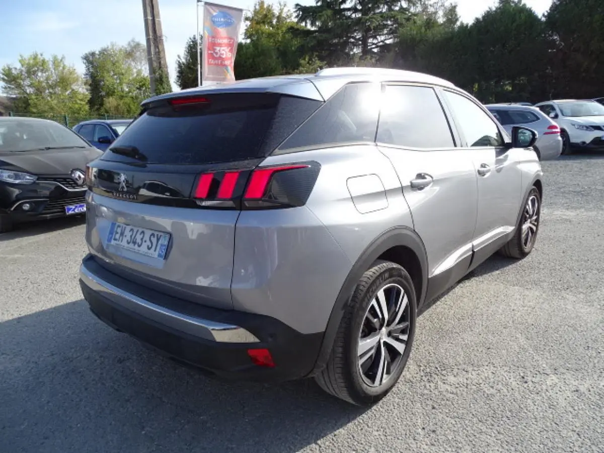 Vue 3/4 arrière droite d'un Peugeot 3008 gris Artense avec barres de toit en aluminium et feux arrière à griffes rouges.