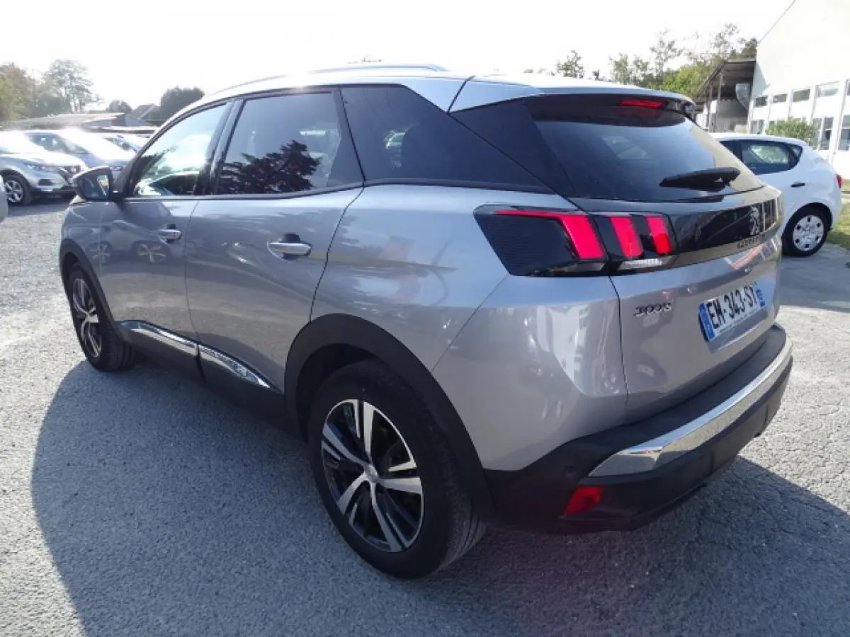Vue 3/4 arrière gauche d'un Peugeot 3008 gris Artense avec barres de toit en aluminium et feux arrière à griffes rouges.