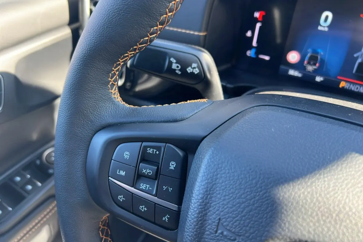 Gros plan sur le volant avec commandes multifonctions du Ford Ranger Wildtrak 2025, cuir noir et surpiqûres orange.