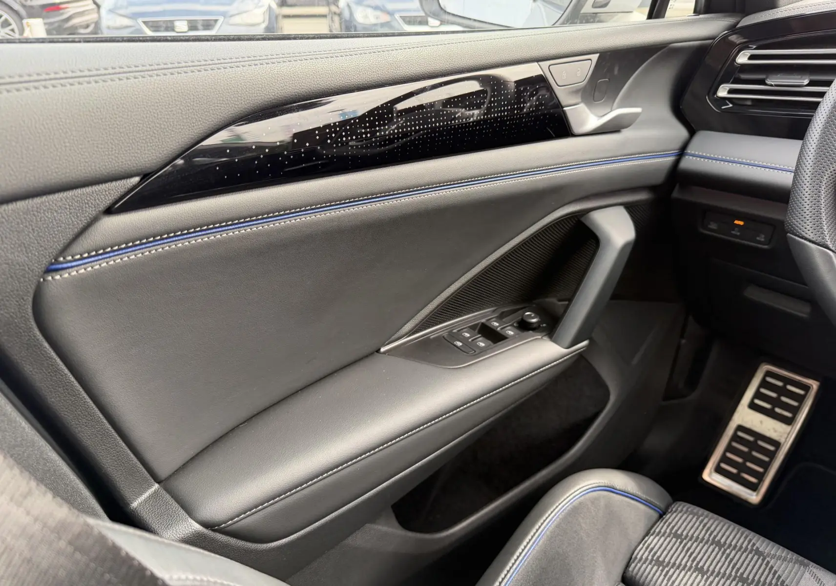 Vue intérieure côté gauche du Volkswagen Tiguan 2025, avec porte en cuir noir, surpiqûres bleues et inserts décoratifs lumineux.